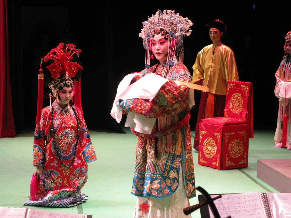 Peking Opera performers in dan (female) role costumes on stage with the musical ensemble